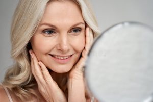 Feliz s mediana edad mujer tocando cara piel mirando en espejo modelo sonriente señora madura mimos disfrutar de cuidado la sana